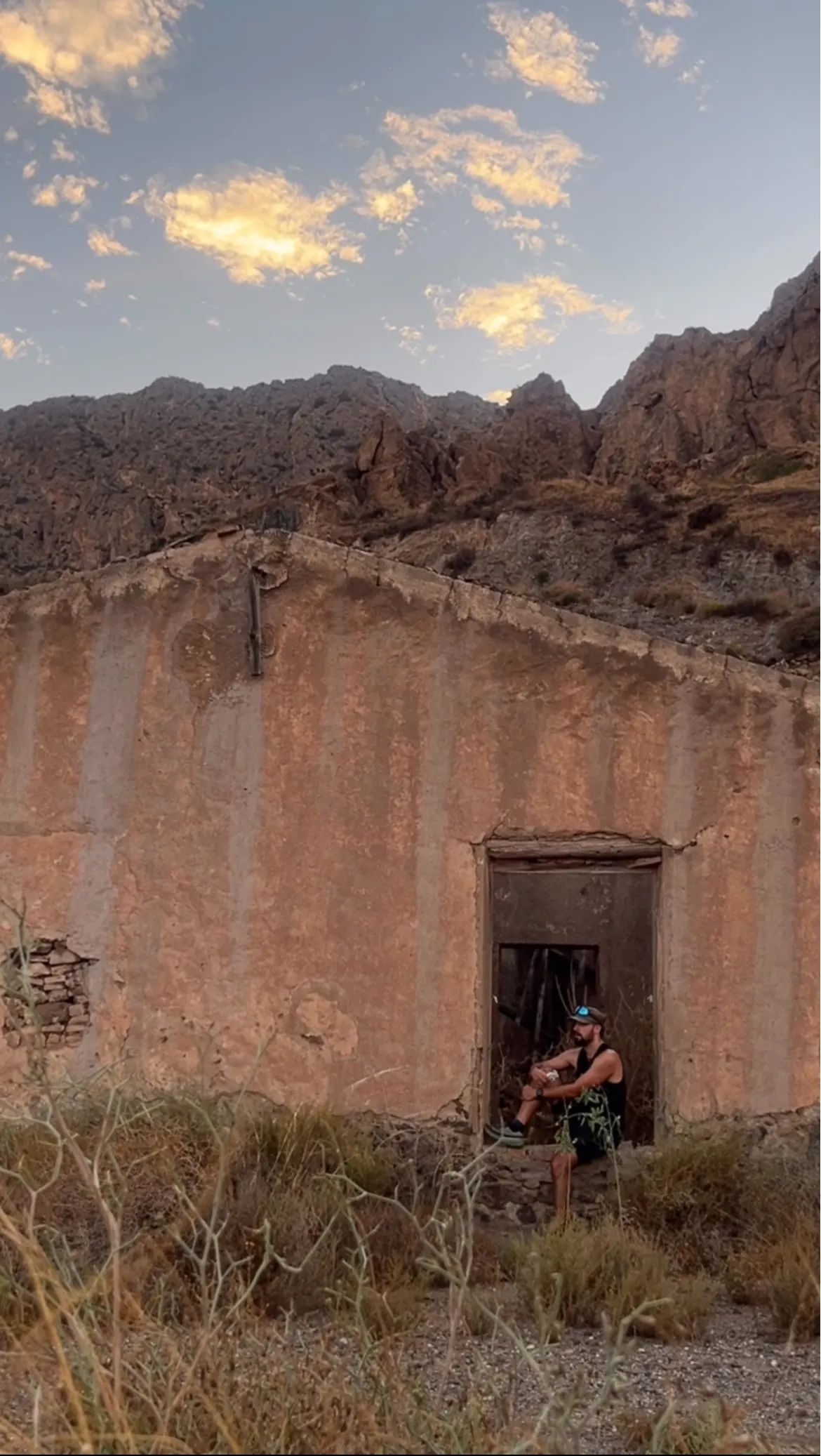 Diego DPL sentado en el umbral de una casa abandonada en la sierra, al atardecer